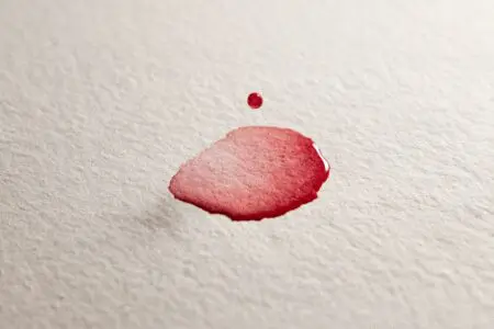Nežna kapljica rjavkasto-rdeče barve na belem papirju ponazarja kako izgleda prva menstruacija