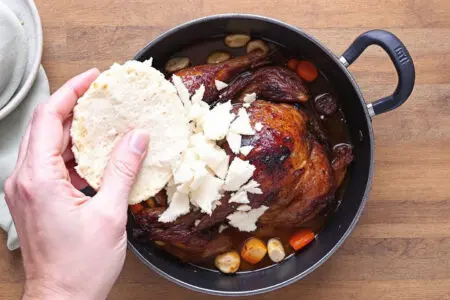 Kako Pripraviti Mlince – Domači Mlinci Korak Za Korakom roke ki lomijo suhe mlince v pekač z mesnim sokom kar ponazarja kako pripraviti mlince